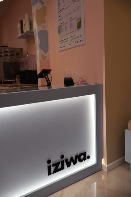 Inside Iziwa, the counter with its lit iziwa sign and the drinks menu on the wall behind